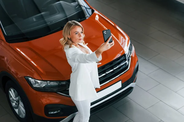 Making selfie. Woman in formal clothes is indoors in the autosalon.