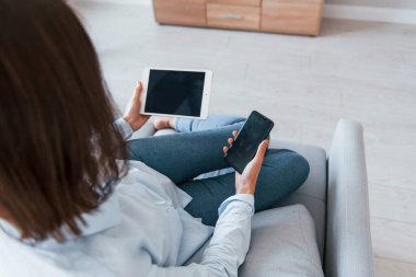 Akıllı telefon ve tablet tutuyor. Genç kadın, gündüz vakti modern evin içinde..