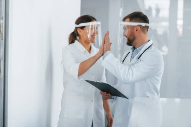Koruyucu maskelerle. Beyaz önlüklü iki doktor klinikte birlikte çalışıyorlar..
