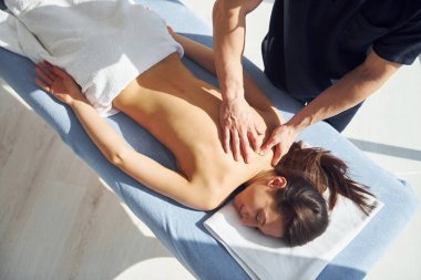 Oda güneş ışınlarıyla aydınlatılıyor. Genç bir kadın, erkek kaplıcada vücuduna masaj yaparken uzanır..