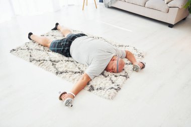 Yorgun yatıyorum. Ellerinde halterlerle. Sıradan giysili komik şişman adam evde..