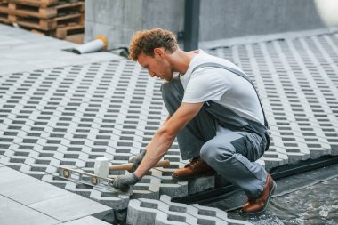 Açık havada iş. Gündüz vakti inşaatta üniformalı genç bir adam çalışıyor..