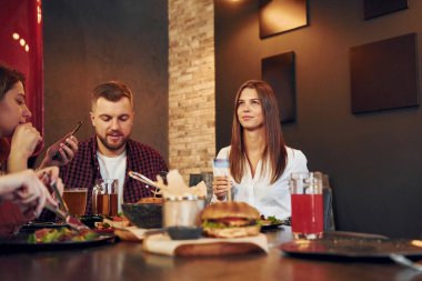Masanın yanında. Bir grup genç arkadaş barda birlikte oturup bira içiyorlar..