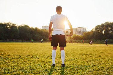 Ayakta duruyor ve topu elinde tutuyor. Genç futbolcu spor sahasında antrenman yapıyor..