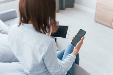 Akıllı telefon ve tablet tutuyor. Genç kadın, gündüz vakti modern evin içinde..