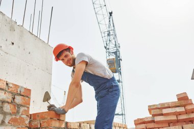 Tuğla taşıyorum. Üniformalı genç inşaat işçisi tamamlanmamış binada meşgul..