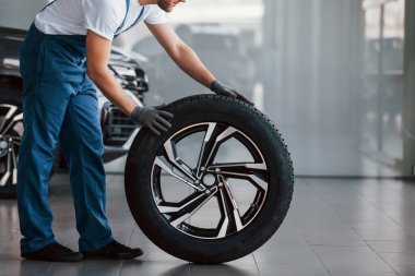 Lastikle. Beyaz gömlekli ve mavi üniformalı genç adam otomobil tamir ediyor..