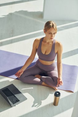 İçki ve dizüstü bilgisayar yerde. Spor elbiseli bir kadın evde yoga yapıyor..
