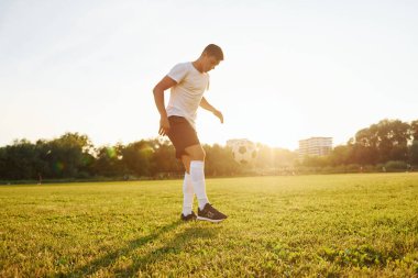 Arka planda orman var. Genç futbolcu spor sahasında antrenman yapıyor..