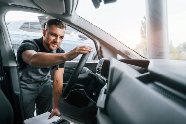 Kalite kontrolü. Üniformalı adam gündüz vakti otosalonda çalışıyor..