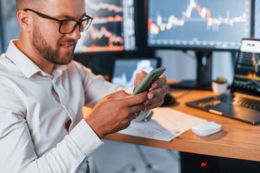 Ellerinde telefonla. Resmi giyinmiş genç işadamı birden fazla ekranla ofiste..