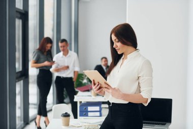 Meslektaşlarının önünde bir kadın. Ofiste resmi giysiler içinde bir grup insan var..