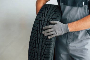 Üniformalı adam gündüz vakti otomatik kanalda çalışıyor. Lastiği ellerinde tutarak.