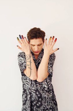 Genç eşcinsel adam stüdyoda duruyor ve kameraya poz veriyor. Yüz parmaklarında çok renkli makyaj malzemeleri var..