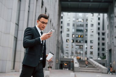 Akıllı telefon kullanarak internet iletişimi. Siyah takım elbiseli ve kravatlı iş adamı şehir dışında..