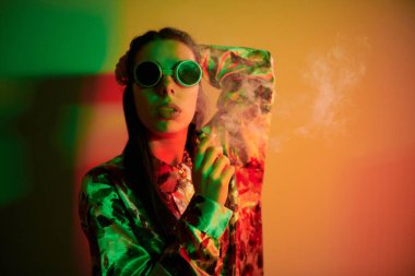 Retro pilot gözlükleriyle. Stüdyoda neon ışığıyla duran şık bir genç kadın..