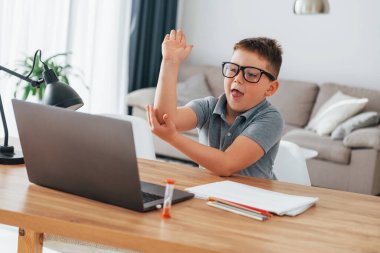 Elini kaldırdı. Küçük çocuk evde dizüstü bilgisayar kullanarak online dersler alıyor..