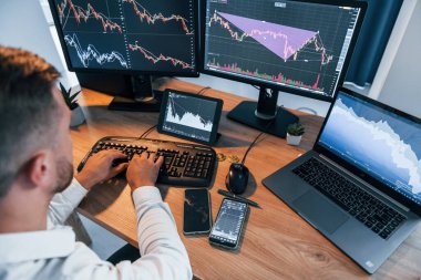 Manzarayı kapat. Resmi giyinmiş genç işadamı birden fazla ekranla ofiste..