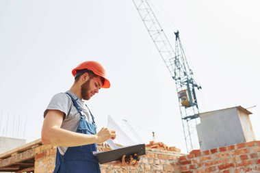 Evrak işleri. Üniformalı genç inşaat işçisi tamamlanmamış binada meşgul..