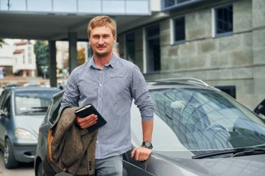 Elinde not defteriyle. Gündüz vakti şehirde gezen bir adam..