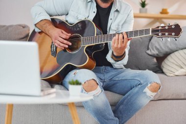 Şarkı yazma süreci. Gündelik giysiler içinde ve akustik gitarlı bir adam içeride..
