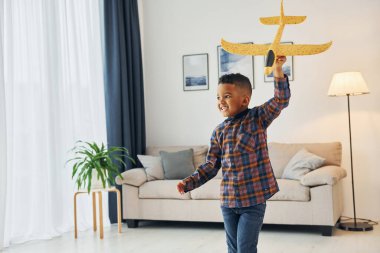 Sarı oyuncak uçağıyla oynuyorum. Neşeli genç çocuk evde yalnız..