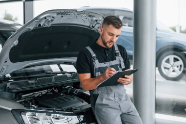 Not defteriyle. Üniformalı adam gündüz vakti otosalonda çalışıyor..