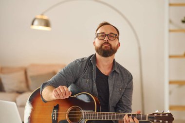 Şarkı yazma becerisi alıştırması yapıyorum. Gündelik giysiler içinde ve akustik gitarlı bir adam içeride..