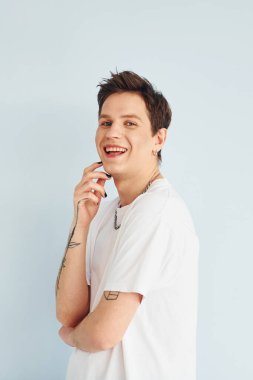 Genç eşcinsel adam stüdyoda duruyor ve kameraya poz veriyor. Sıradan beyaz gömlekli..