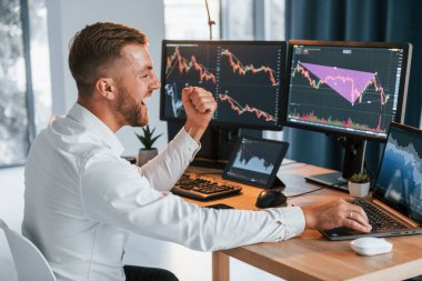 Laptop kullanıyorum. Resmi giyinmiş genç işadamı birden fazla ekranla ofiste..