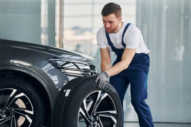 Tekerlek değiştirme. Beyaz gömlekli ve mavi üniformalı genç adam otomobil tamir ediyor..