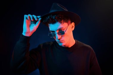 Şapka ve gözlüklerle. Neon ışıkları. Genç Avrupalı adam karanlık stüdyoda..