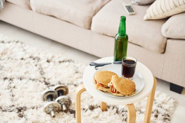 Hamburger ve bira masada. Dambıllar yere..