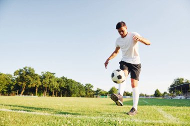 Yaz gündüz vakti. Genç futbolcu spor sahasında antrenman yapıyor..