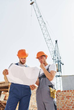 Okuma planı. Üniformalı iki genç inşaat işçisi tamamlanmamış binada meşgul..