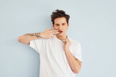 Genç eşcinsel adam stüdyoda duruyor ve kameraya poz veriyor. Dudaklar kırmızı rujla.