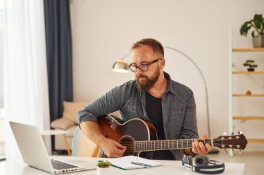 Bazı fikirler yazıyorum. Gündelik giysiler içinde ve akustik gitarlı bir adam içeride..