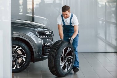 Tekerlek değiştirme. Beyaz gömlekli ve mavi üniformalı genç adam otomobil tamir ediyor..