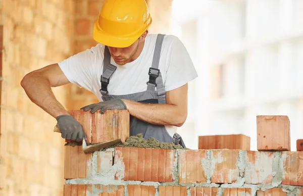 Tuğla döşemesi. Gündüz vakti inşaatta üniformalı genç bir adam çalışıyor..