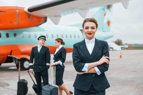 With luggage. Aircraft crew in work uniform is together outdoors near plane.