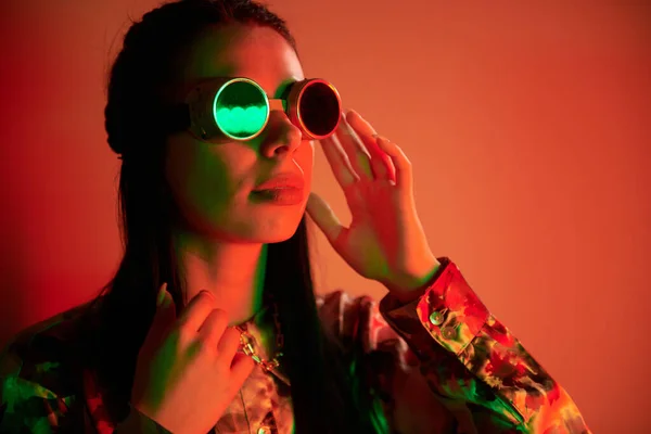 In retro pilot glasses. Fashionable young woman standing in the studio with neon light.