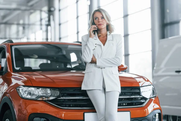Using phone. Woman in formal clothes is indoors in the autosalon.