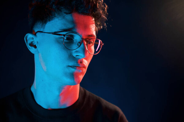 Against black background. Neon lighting. Young european man is in the dark studio.