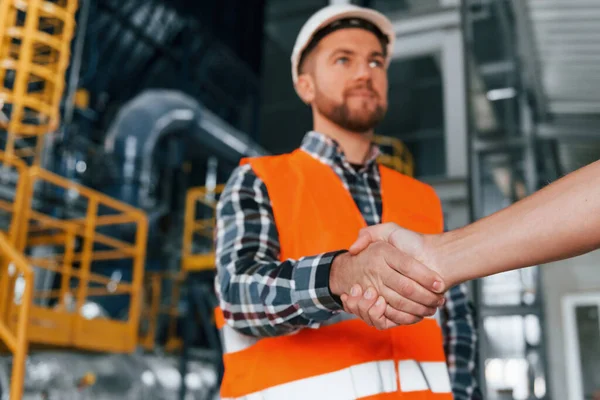 Making handshake with customer. Construction worker in uniform is in the factory.