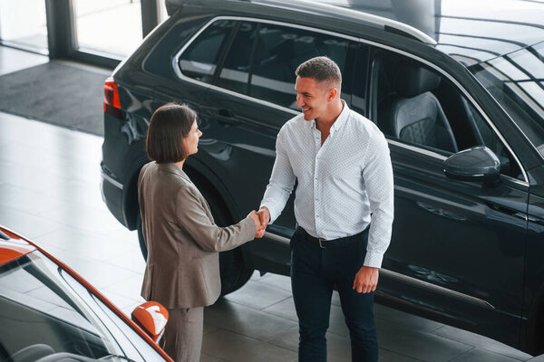 Doing handshake. Man in formal wear helping customer with choice of the automobile.