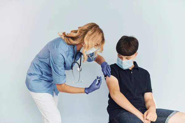 Doctor in uniform making vaccination to the boy in black shirt.
