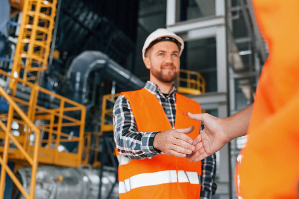 Making handshake with customer. Construction worker in uniform is in the factory.