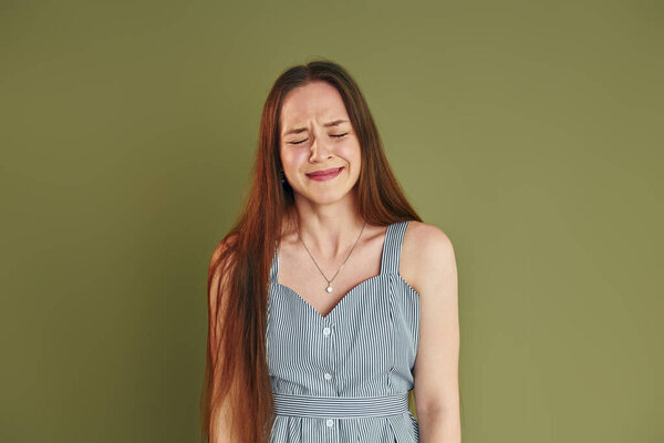 Young woman in casual clothes is crying while standing indoors in the studio.