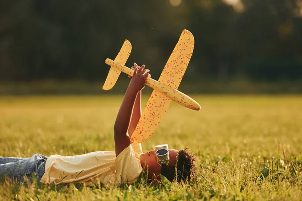 草の上におもちゃの飛行機で横になった アフリカ系アメリカ人の子供は夏の昼間にフィールドで楽しんでいます — ストック写真