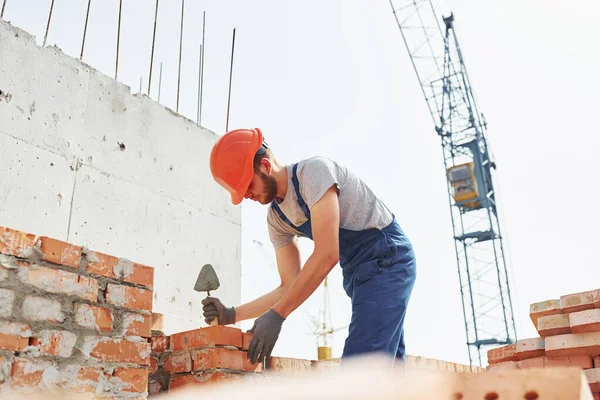 Young construction worker in uniform is busy at the unfinished building.